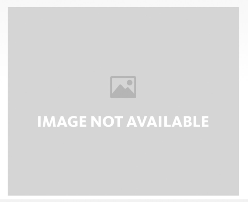 Seascape depicting a large iceberg rising from the water before a coastline with a sailing boat approaching in front.