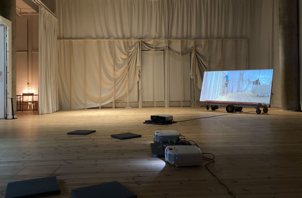 Installation view, Essence of hybridity (2022), laminated veneer, Molton curtain, wallboard trolley, off-painted photograph, text, light, video projection on particle board, 4 min